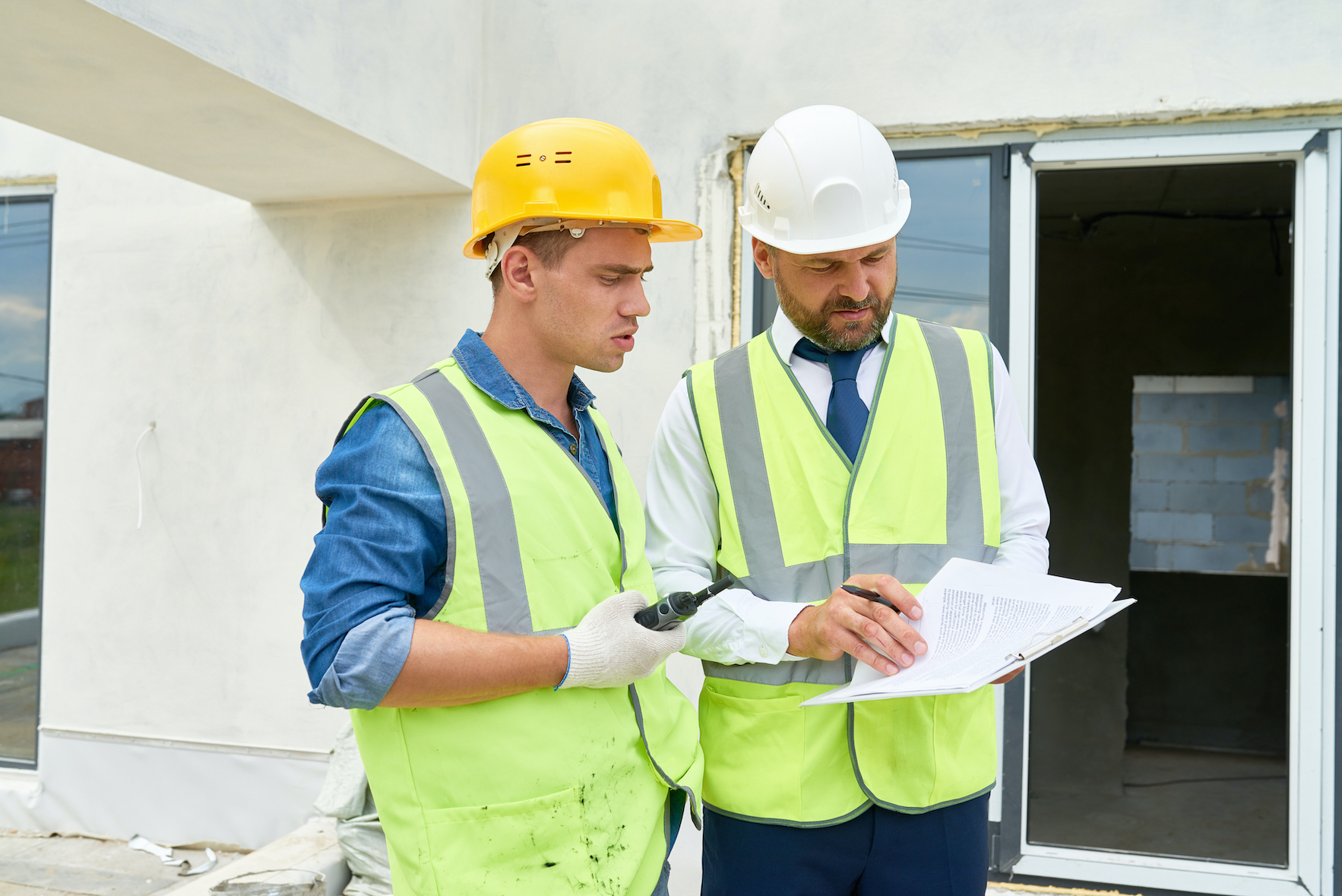 Portrait of foreman and supervisor discussing construction documents on site, both wearing hardhats and reflective vests